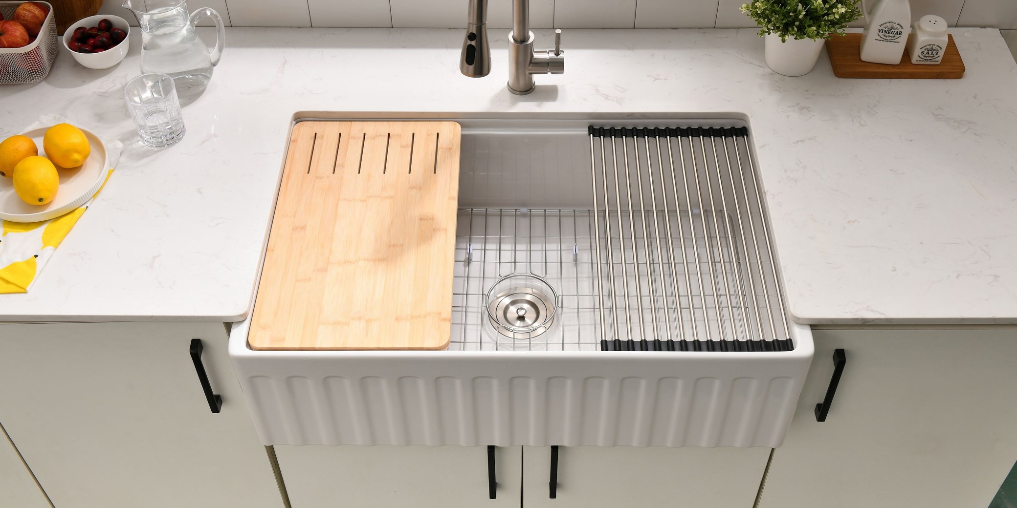 Overhead view of a white fluted fireclay workstation farmhouse sink set in a marble worktop, with a bamboo cutting board, roll-up rack and bottom grid in place showing the full outer width