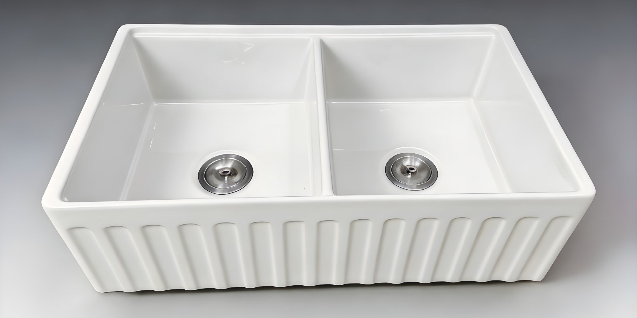 Top view of a white fireclay double-bowl farmhouse workstation sink with a vertically fluted apron front facing the viewer, two stainless basket strainers visible, on a neutral grey background
