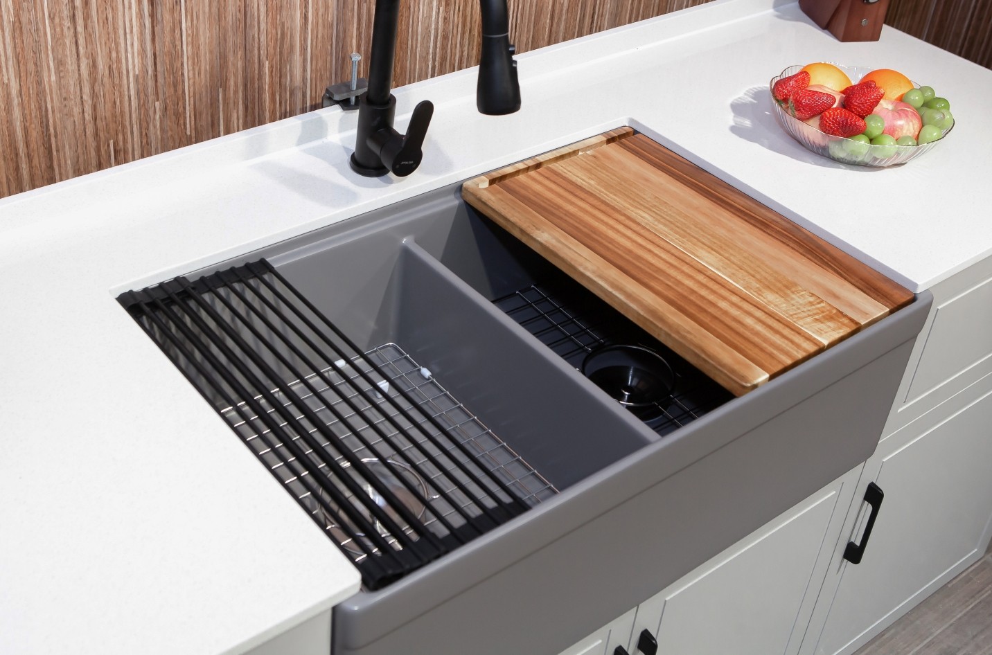 Grey fireclay double bowl farmhouse workstation sink with a sliding wood cutting board, roll-up drying rack and bottom grid riding the integrated ledge