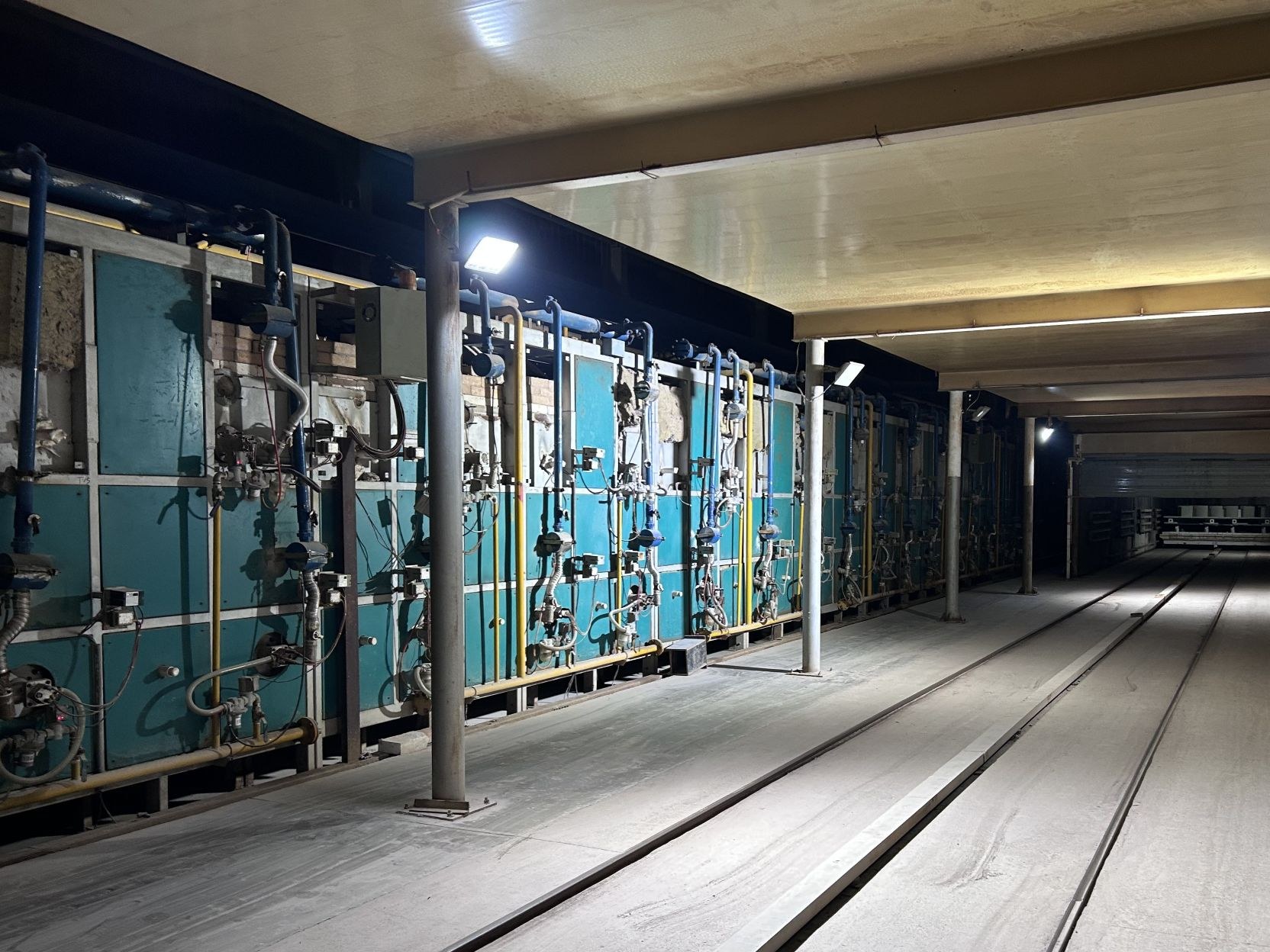Ceramic ware entering a gas-fired tunnel kiln during the firing cycle, with the cooling section behind