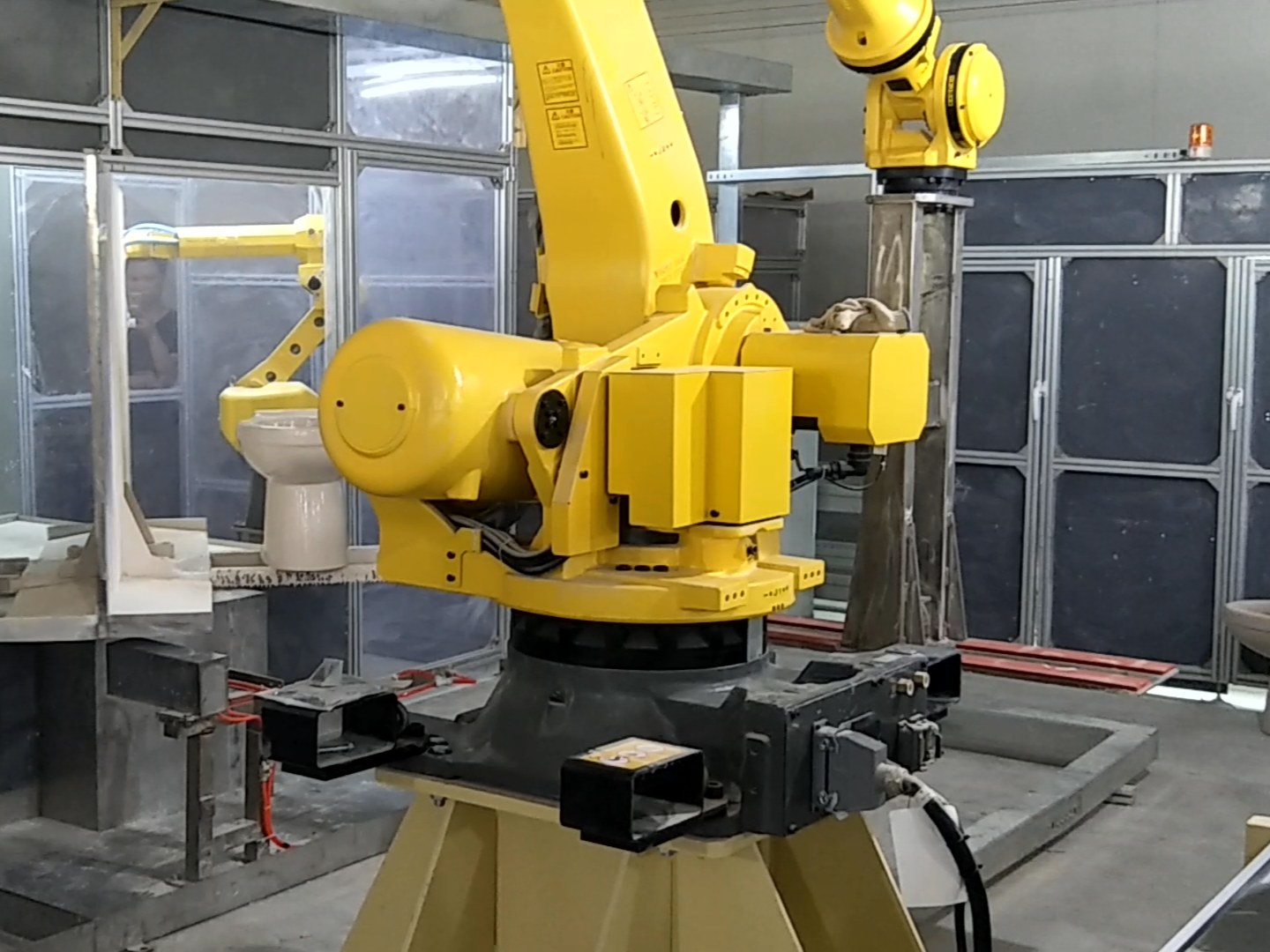 Robotic glazing arm applying a controlled glaze layer to a ceramic sink body